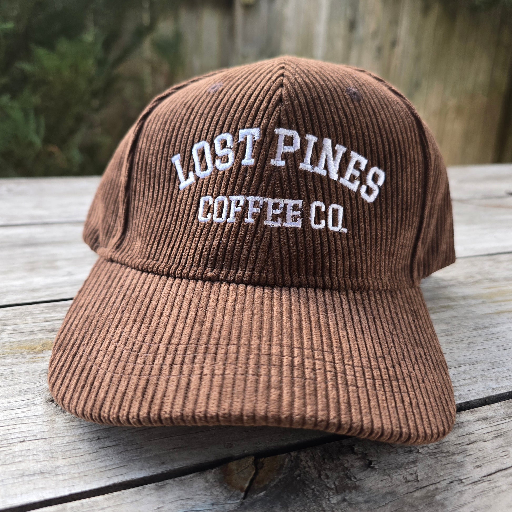 Brown corduroy cap with 'Lost Pines Coffee Co.' text on a wooden surface
