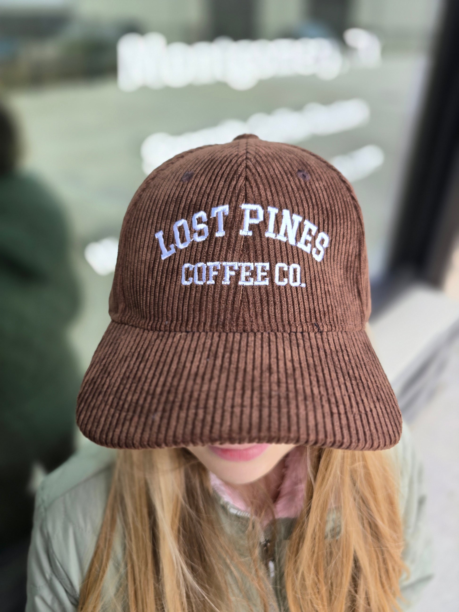 Brown knit cap with 'Lost Pines Coffee Co.' text worn by a person.